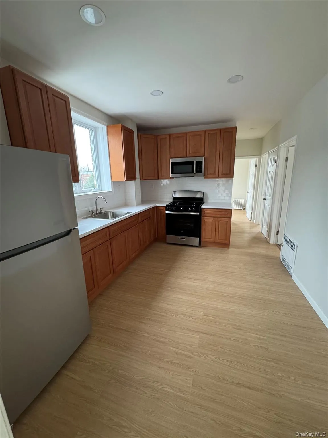 Kitchen with stainless steel appliances, light countertops, brown cabinets, light wood-style flooring, and tasteful backsplash Kitchen with stainless steel appliances, light countertops, brown cabinets, light wood-style flooring, and tasteful backsplash
