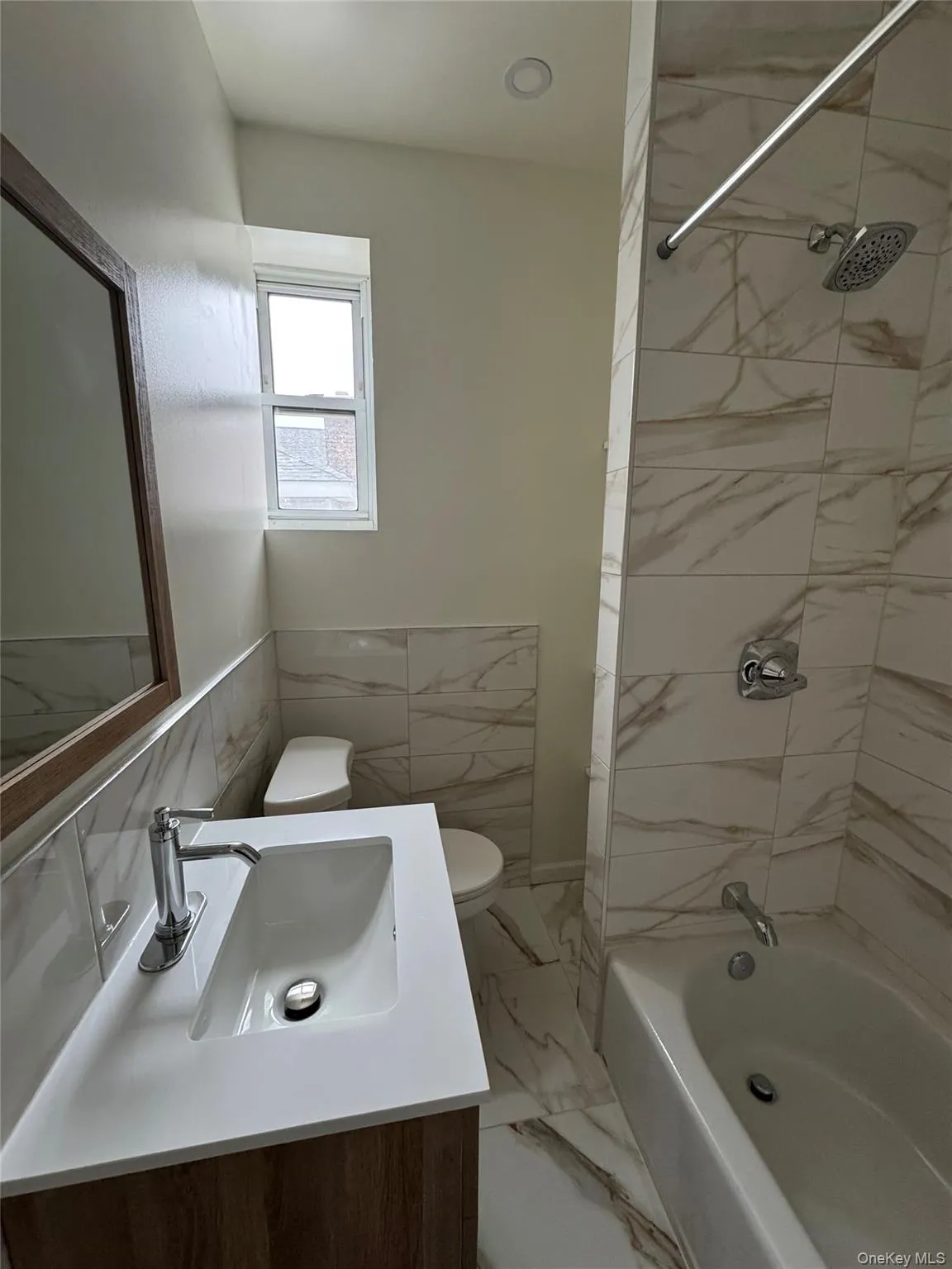 Full bath featuring shower / bath combination, light marble finish floors, vanity, and wainscoting Full bath featuring shower / bath combination, light marble finish floors, vanity, and wainscoting