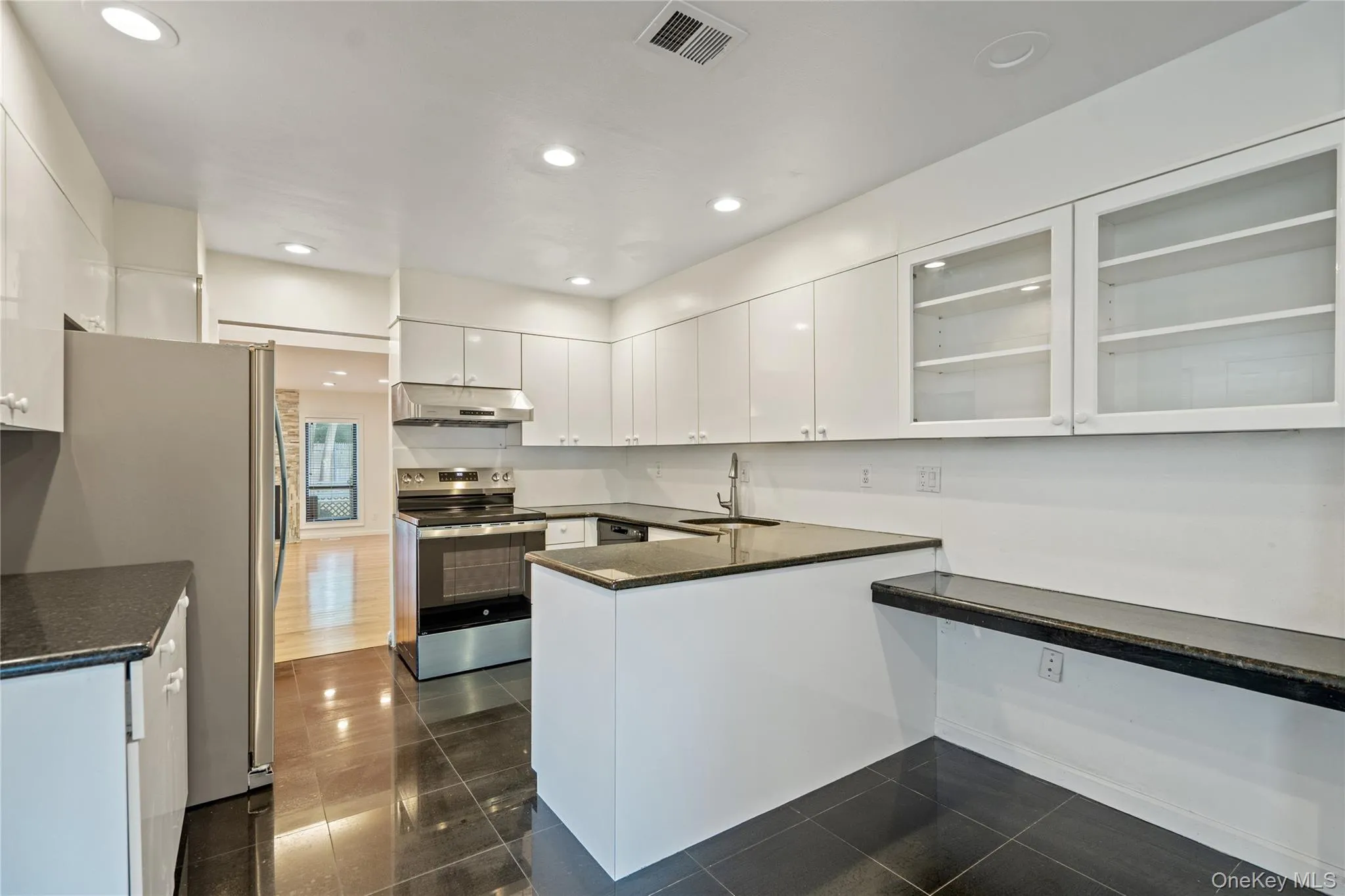 Kitchen with stainless steel appliances, a peninsula, white cabinetry, glass insert cabinets, and dark stone counters Kitchen with stainless steel appliances, a peninsula, white cabinetry, glass insert cabinets, and dark stone counters