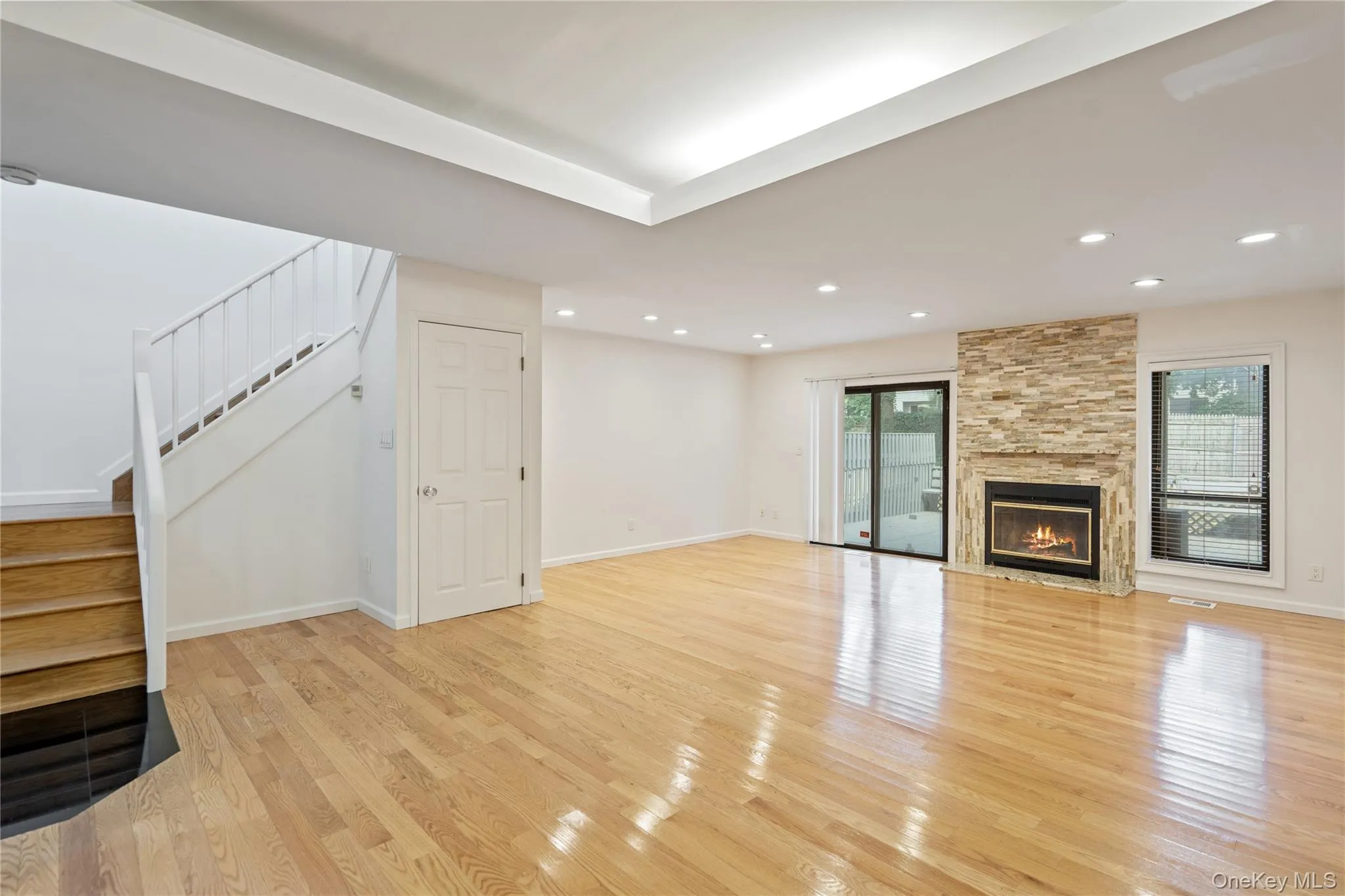 Unfurnished living room with stairway, a stone fireplace, light wood finished floors, and recessed lighting Unfurnished living room with stairway, a stone fireplace, light wood finished floors, and recessed lighting