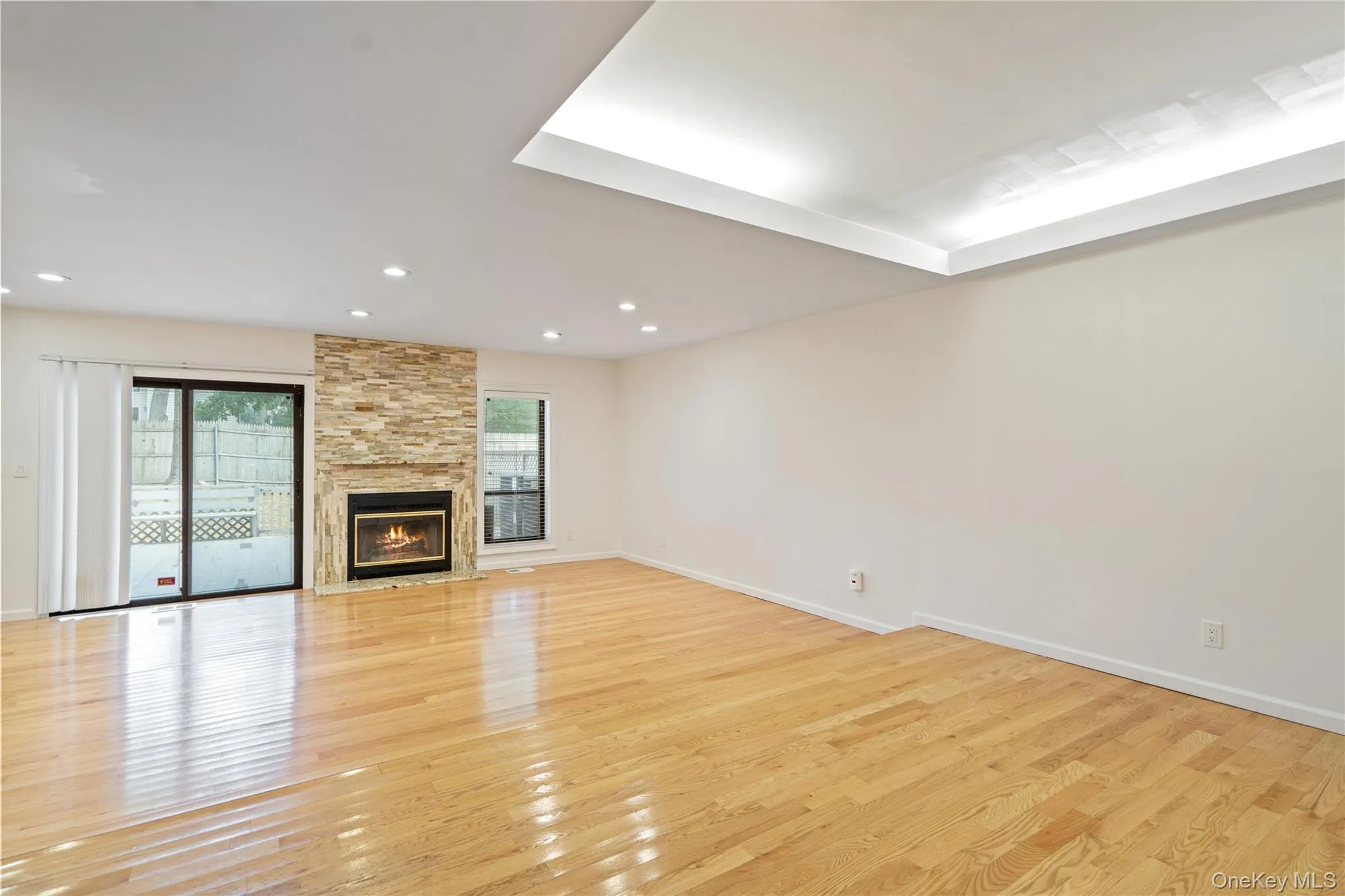 Unfurnished living room featuring light wood finished floors, a stone fireplace, and recessed lighting Unfurnished living room featuring light wood finished floors, a stone fireplace, and recessed lighting