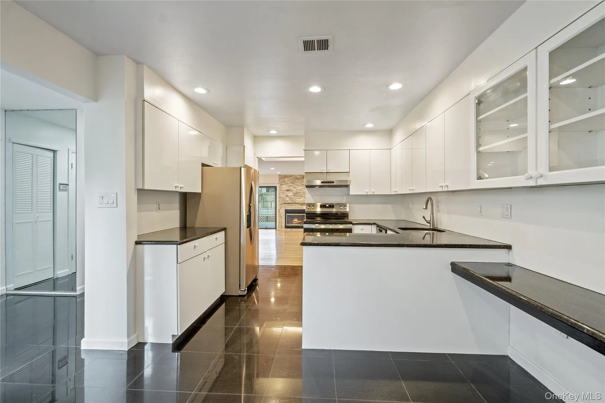 Kitchen with glass insert cabinets, stainless steel appliances, white cabinetry, a peninsula, and dark stone counters Kitchen with glass insert cabinets, stainless steel appliances, white cabinetry, a peninsula, and dark stone counters