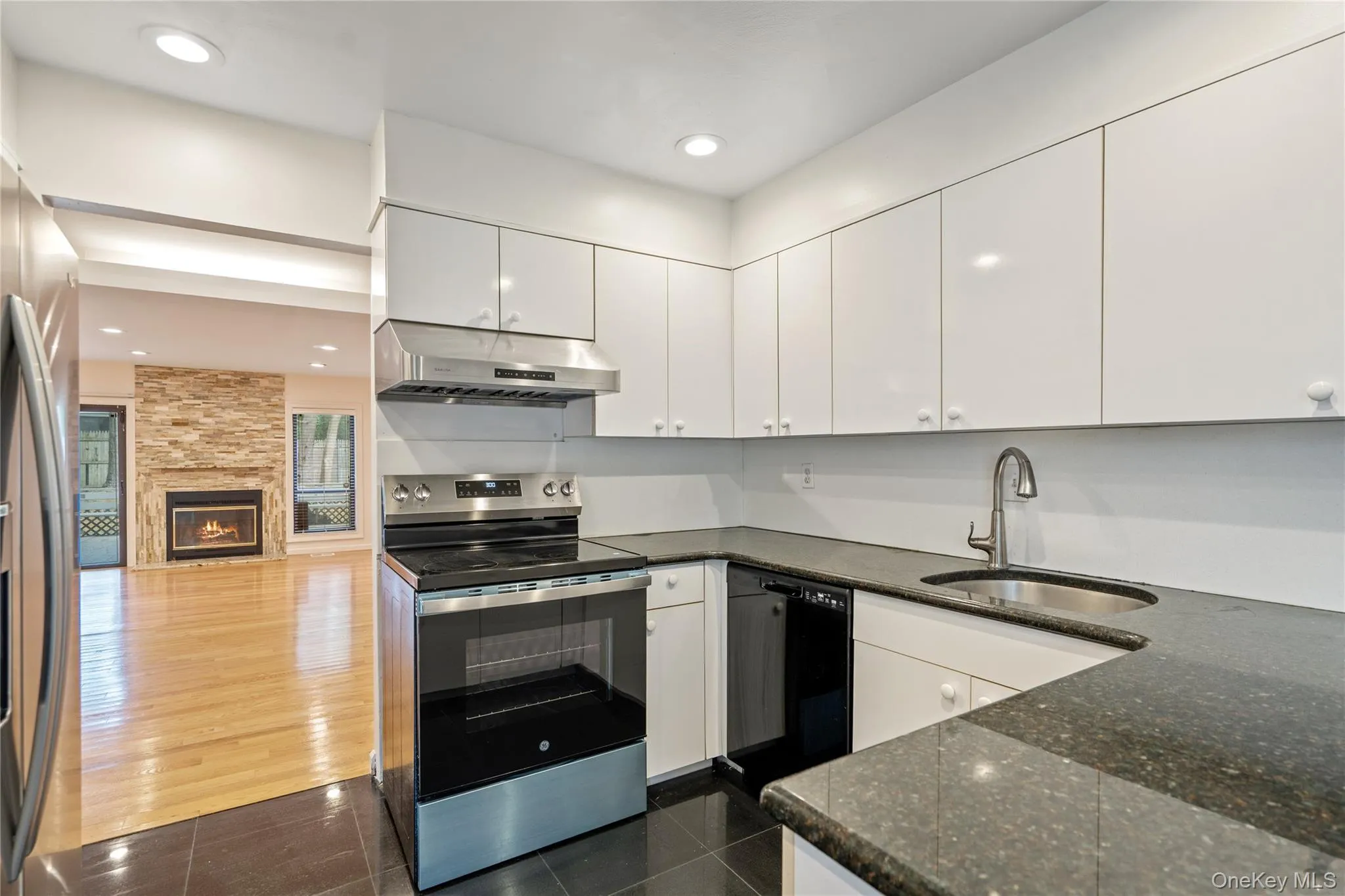 Kitchen featuring appliances with stainless steel finishes, white cabinets, under cabinet range hood, dark stone counters, and recessed lighting Kitchen featuring appliances with stainless steel finishes, white cabinets, under cabinet range hood, dark stone counters, and recessed lighting