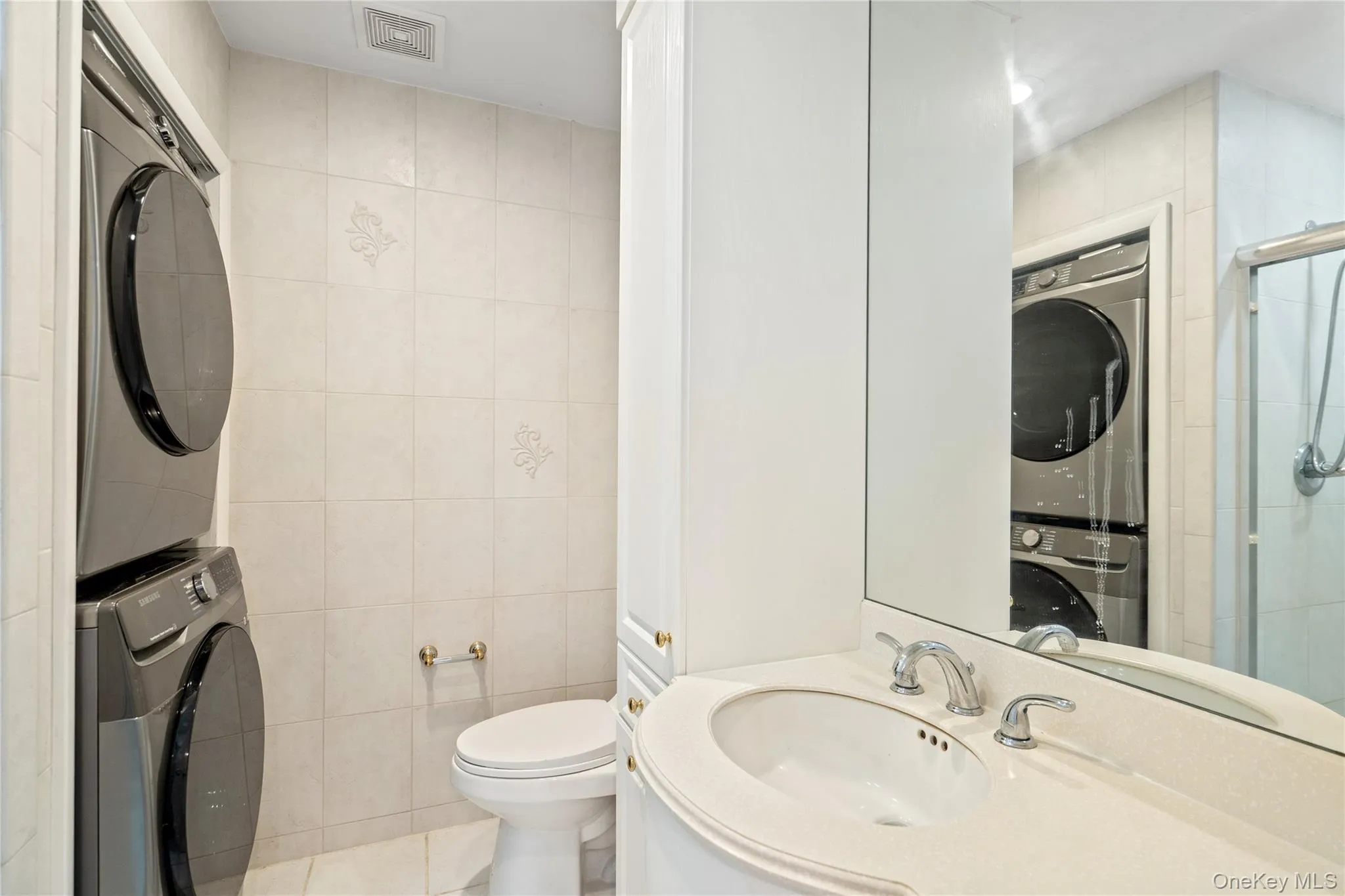 Bathroom featuring stacked washer / drying machine, tile walls, vanity, a stall shower, and tile patterned floors Bathroom featuring stacked washer / drying machine, tile walls, vanity, a stall shower, and tile patterned floors