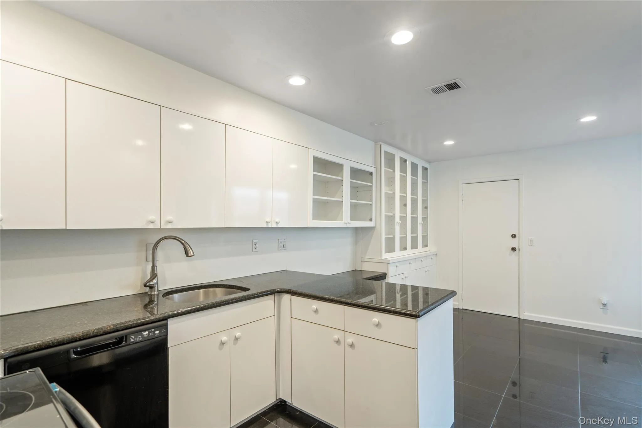 Kitchen featuring glass insert cabinets, black appliances, recessed lighting, a peninsula, and white cabinets Kitchen featuring glass insert cabinets, black appliances, recessed lighting, a peninsula, and white cabinets