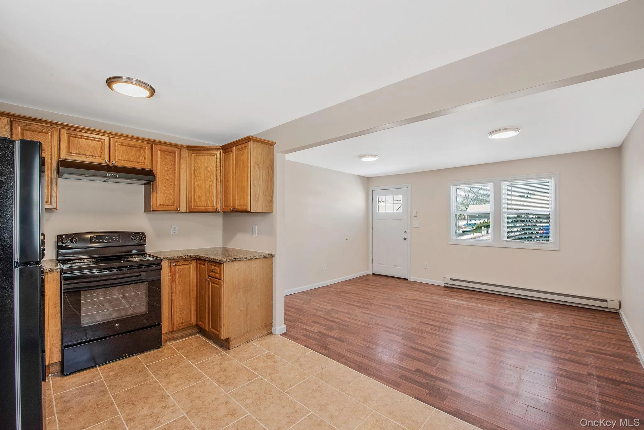 Kitchen featuring black appliances, light tile patterned floors, baseboard heating, under cabinet range hood, and dark stone countertops Kitchen featuring black appliances, light tile patterned floors, baseboard heating, under cabinet range hood, and dark stone countertops