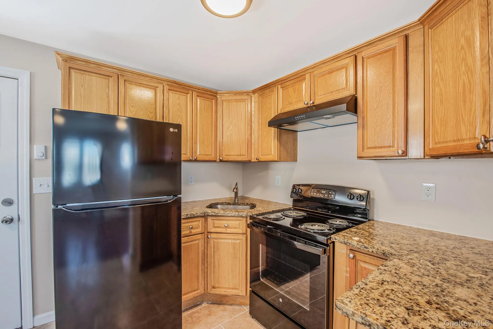 Kitchen featuring black appliances, light stone countertops, under cabinet range hood, and light tile patterned floors Kitchen featuring black appliances, light stone countertops, under cabinet range hood, and light tile patterned floors