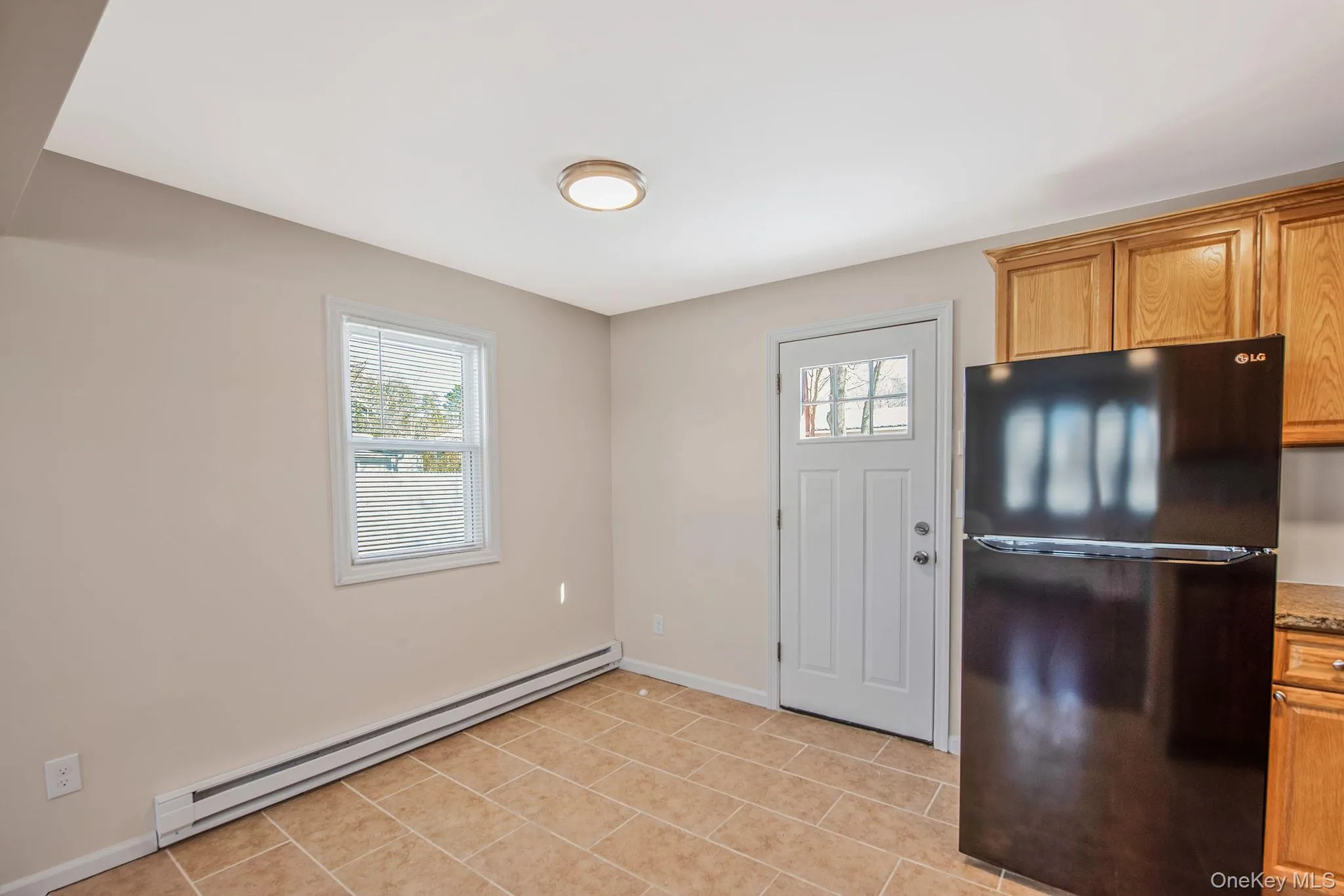 Kitchen with freestanding refrigerator, a baseboard heating unit, plenty of natural light, and brown cabinetry Kitchen with freestanding refrigerator, a baseboard heating unit, plenty of natural light, and brown cabinetry