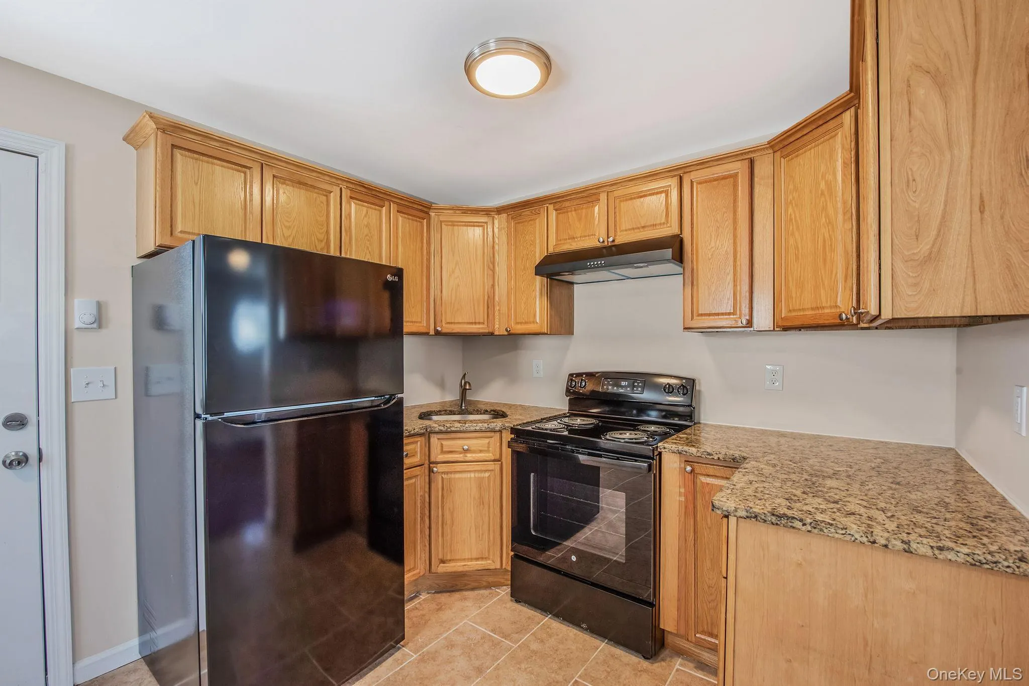 Kitchen with black appliances, light stone counters, light tile patterned flooring, and under cabinet range hood Kitchen with black appliances, light stone counters, light tile patterned flooring, and under cabinet range hood