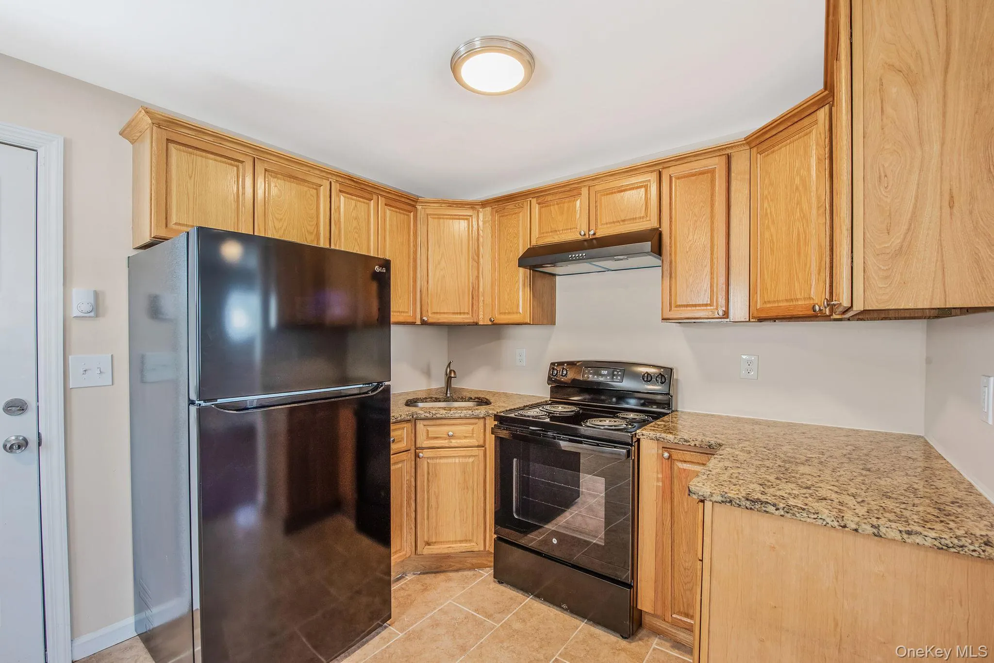 Kitchen with black appliances, light stone counters, under cabinet range hood, light tile patterned floors, and light brown cabinets Kitchen with black appliances, light stone counters, under cabinet range hood, light tile patterned floors, and light brown cabinets