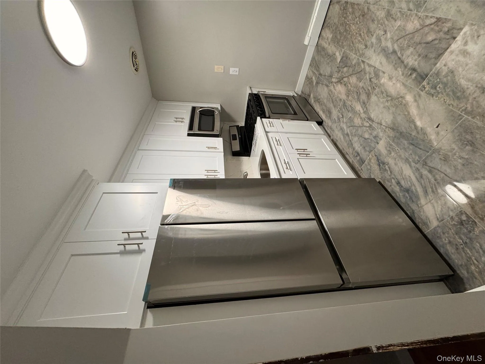 Kitchen with appliances with stainless steel finishes, white cabinets, a baseboard radiator, and light marble finish flooring Kitchen with appliances with stainless steel finishes, white cabinets, a baseboard radiator, and light marble finish flooring