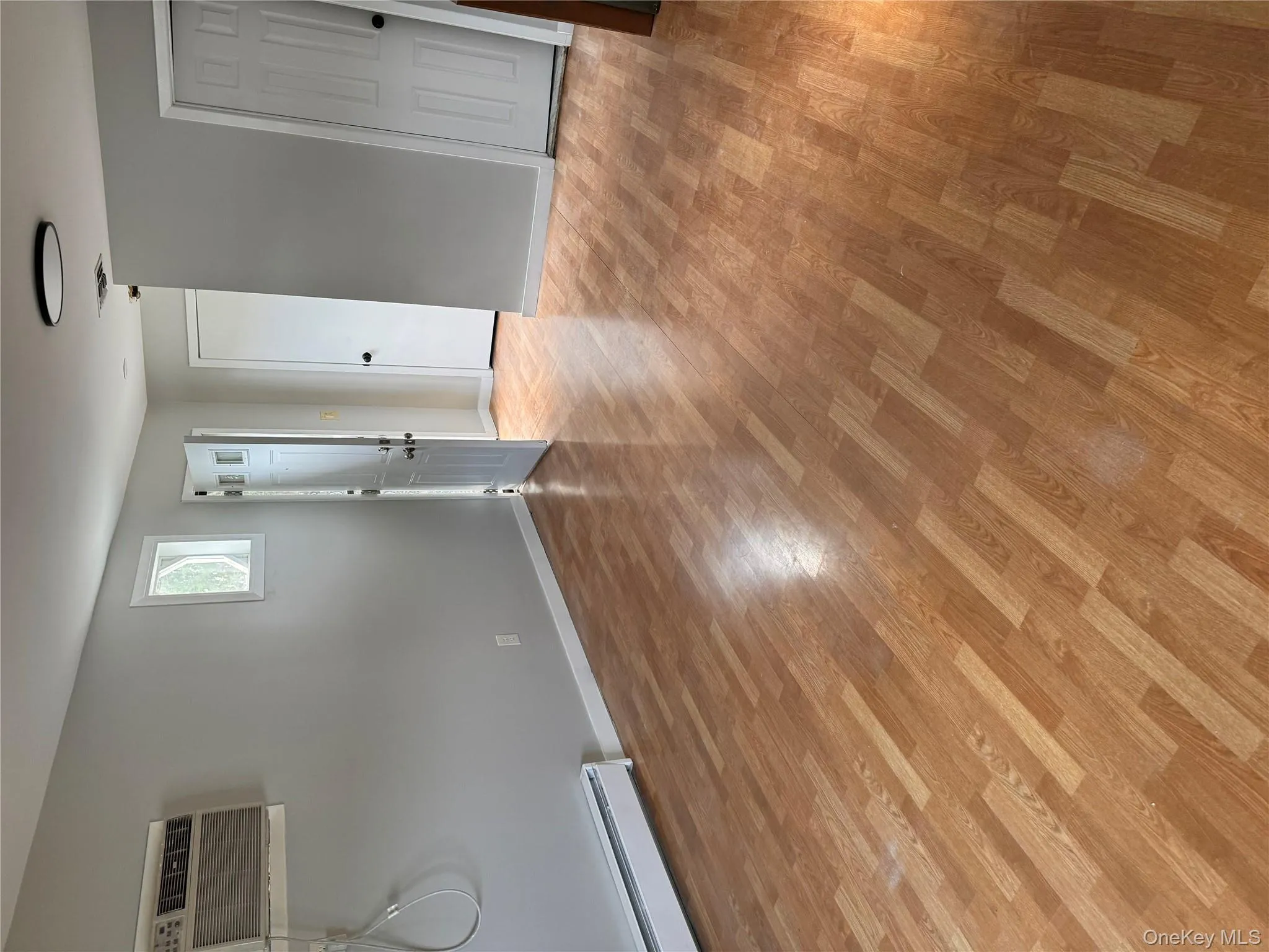 Spare room with a baseboard radiator, light wood-style floors, and an AC wall unit Spare room with a baseboard radiator, light wood-style floors, and an AC wall unit