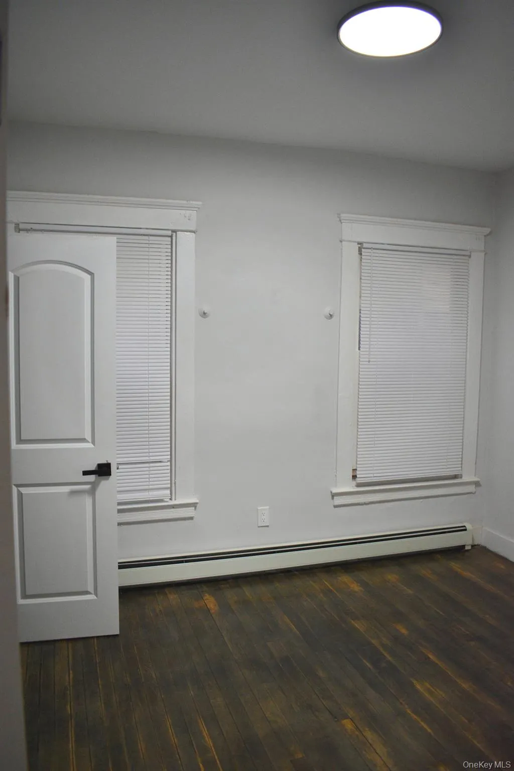 Empty room with a baseboard radiator and dark wood-style floors Empty room with a baseboard radiator and dark wood-style floors