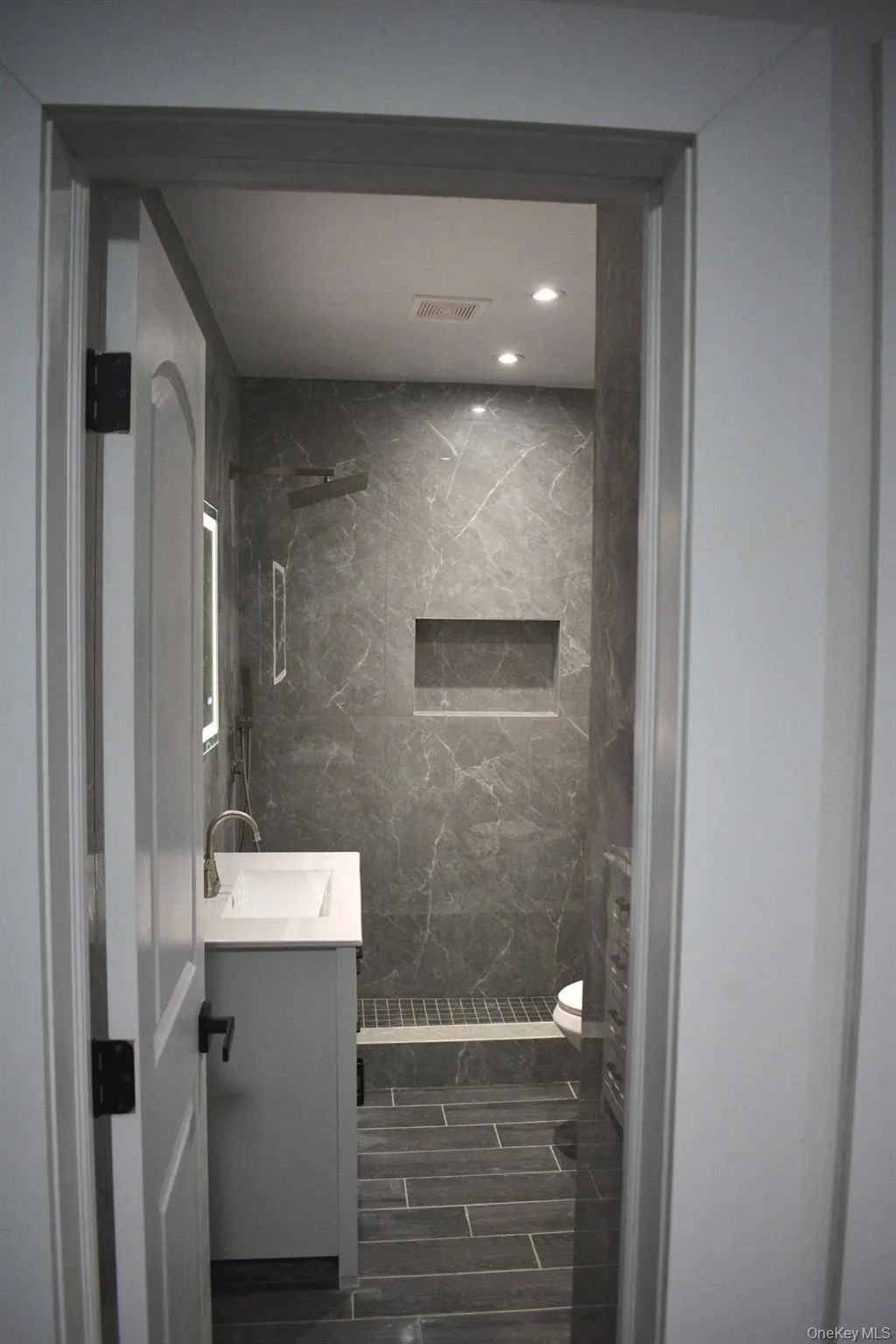 Bathroom featuring a marble finish shower, vanity, and recessed lighting Bathroom featuring a marble finish shower, vanity, and recessed lighting