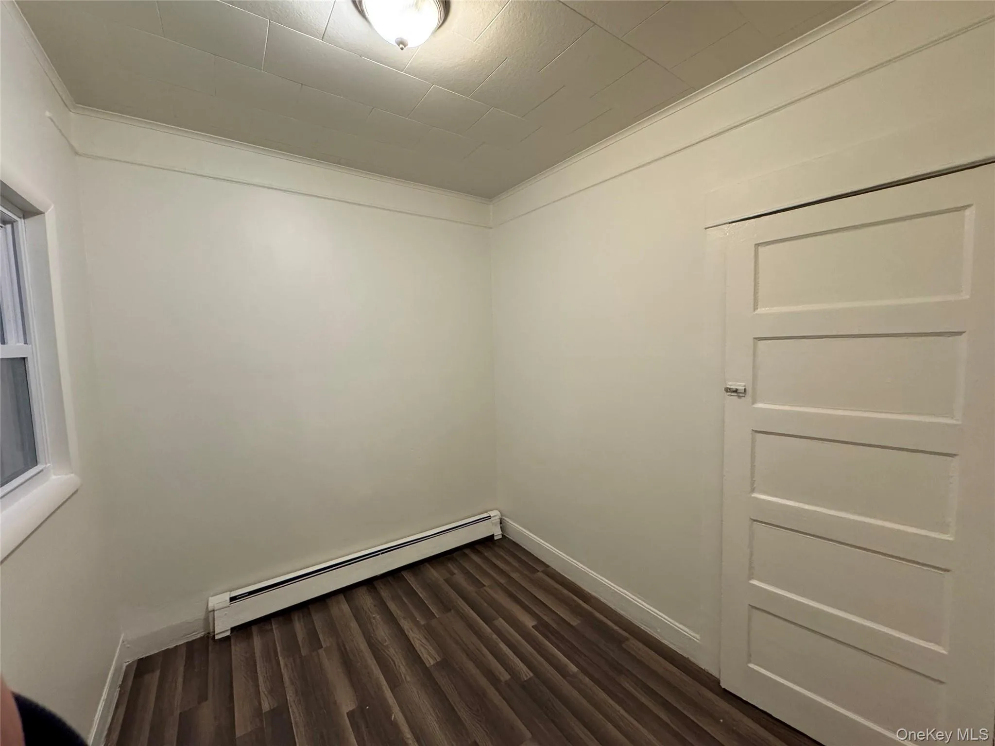 Empty room with dark wood-style floors, a baseboard heating unit, and crown molding Empty room with dark wood-style floors, a baseboard heating unit, and crown molding