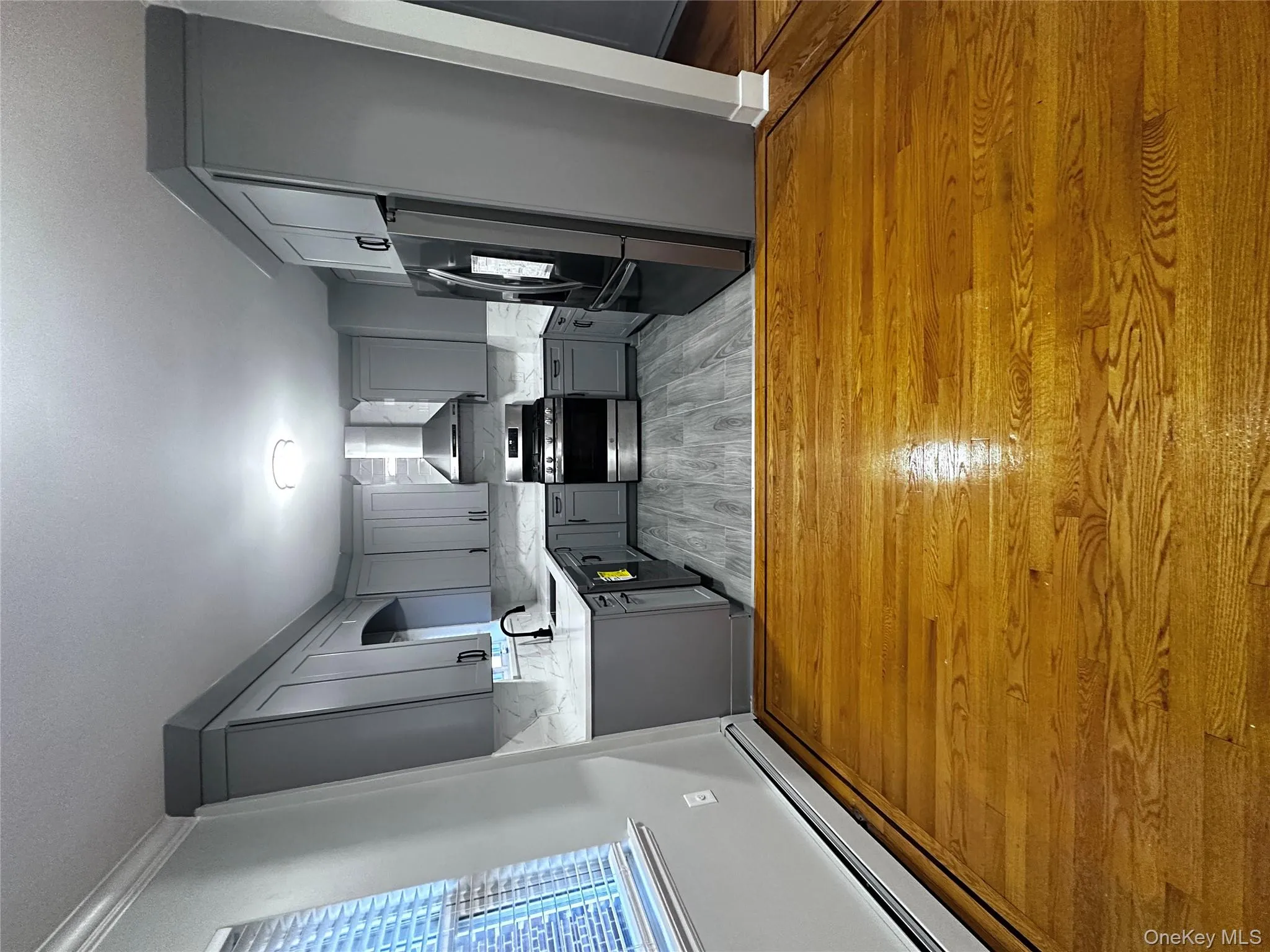 Kitchen featuring gray cabinetry, fridge, a baseboard heating unit, range, and exhaust hood Kitchen featuring gray cabinetry, fridge, a baseboard heating unit, range, and exhaust hood