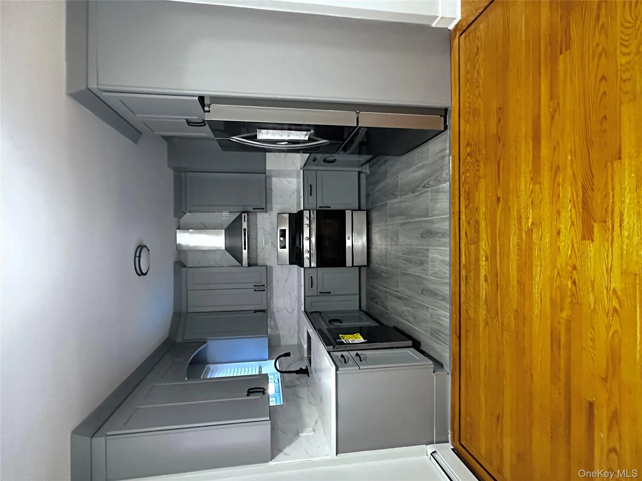 Kitchen with gray cabinets, stainless steel gas range oven, black refrigerator, ventilation hood, and light wood finished floors Kitchen with gray cabinets, stainless steel gas range oven, black refrigerator, ventilation hood, and light wood finished floors