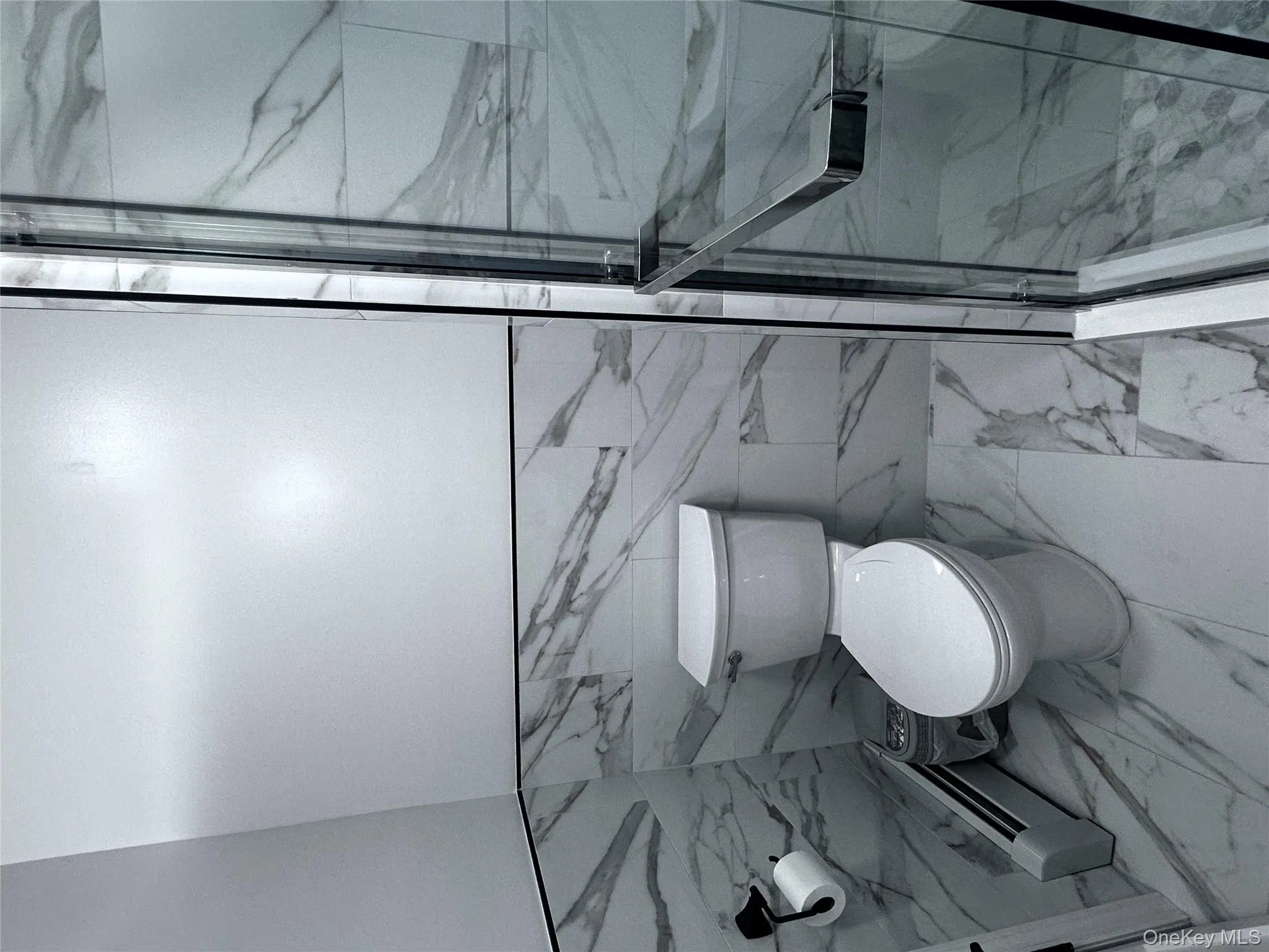 Full bathroom with tile walls, marble look tile flooring, a wainscoted wall, baseboard heating, and a marble finish shower Full bathroom with tile walls, marble look tile flooring, a wainscoted wall, baseboard heating, and a marble finish shower