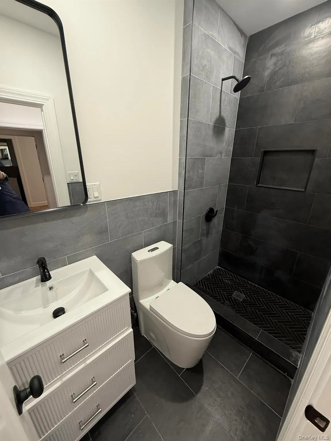 Full bathroom with a tile shower, tile walls, toilet, vanity, and tile patterned flooring Full bathroom with a tile shower, tile walls, toilet, vanity, and tile patterned flooring