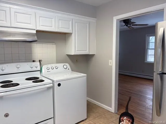 Laundry area featuring washer / dryer, baseboard heating, a ceiling fan, and light tile patterned floors Laundry area featuring washer / dryer, baseboard heating, a ceiling fan, and light tile patterned floors