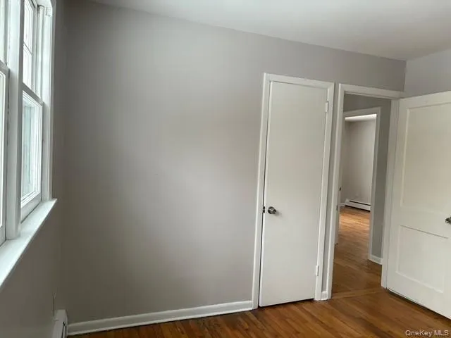 Unfurnished bedroom featuring dark wood finished floors and a baseboard radiator Unfurnished bedroom featuring dark wood finished floors and a baseboard radiator