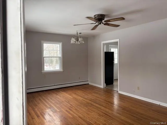Empty room featuring a baseboard heating unit, plenty of natural light, hardwood / wood-style floors, and a chandelier Empty room featuring a baseboard heating unit, plenty of natural light, hardwood / wood-style floors, and a chandelier