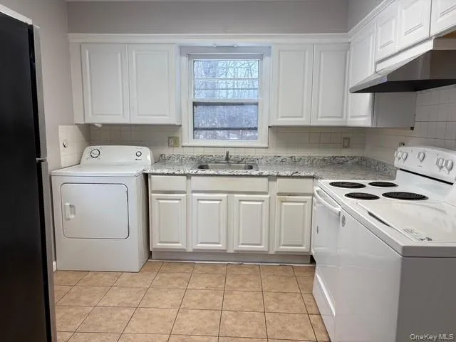 Kitchen featuring washer / clothes dryer, white electric stove, freestanding refrigerator, under cabinet range hood, and white cabinets Kitchen featuring washer / clothes dryer, white electric stove, freestanding refrigerator, under cabinet range hood, and white cabinets