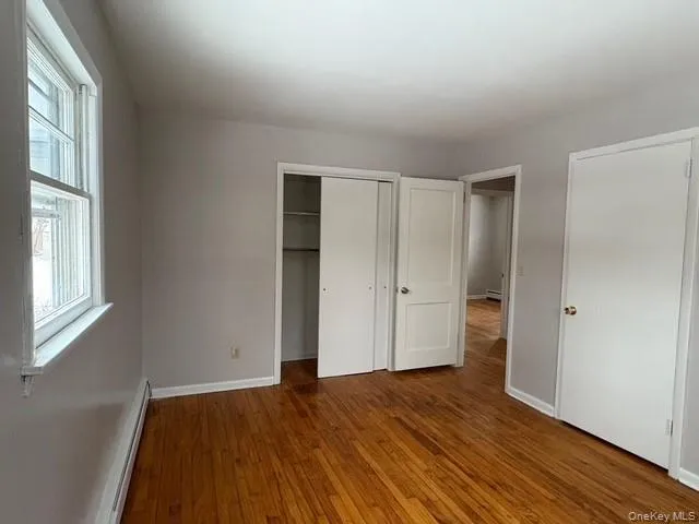 Unfurnished bedroom featuring a baseboard radiator, hardwood / wood-style floors, and a closet Unfurnished bedroom featuring a baseboard radiator, hardwood / wood-style floors, and a closet