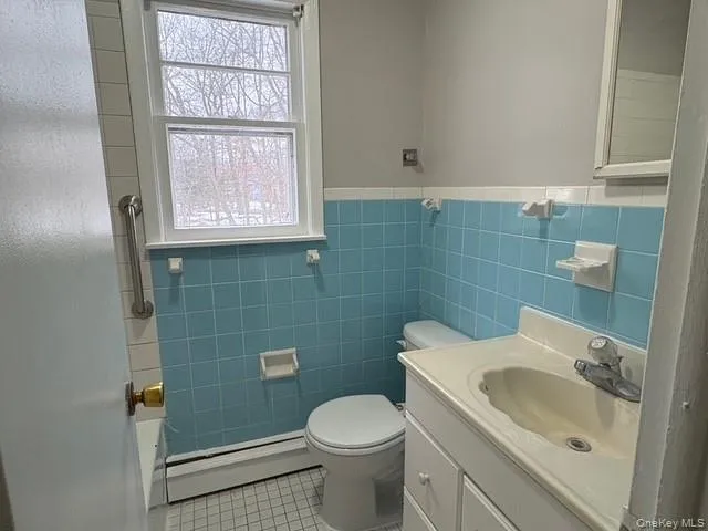 Bathroom featuring vanity, baseboard heating, light tile patterned floors, wainscoting, and tile walls Bathroom featuring vanity, baseboard heating, light tile patterned floors, wainscoting, and tile walls