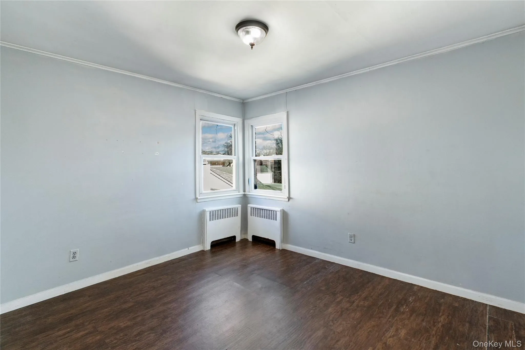Unfurnished room with dark wood-style flooring, radiator heating unit, and ornamental molding Unfurnished room with dark wood-style flooring, radiator heating unit, and ornamental molding