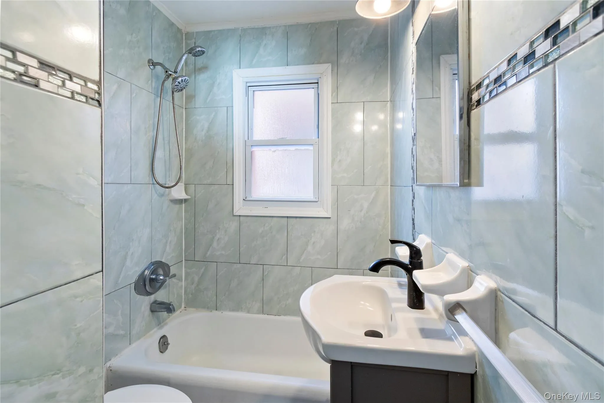 Bathroom featuring vanity, shower / bathtub combination, and tile walls Bathroom featuring vanity, shower / bathtub combination, and tile walls