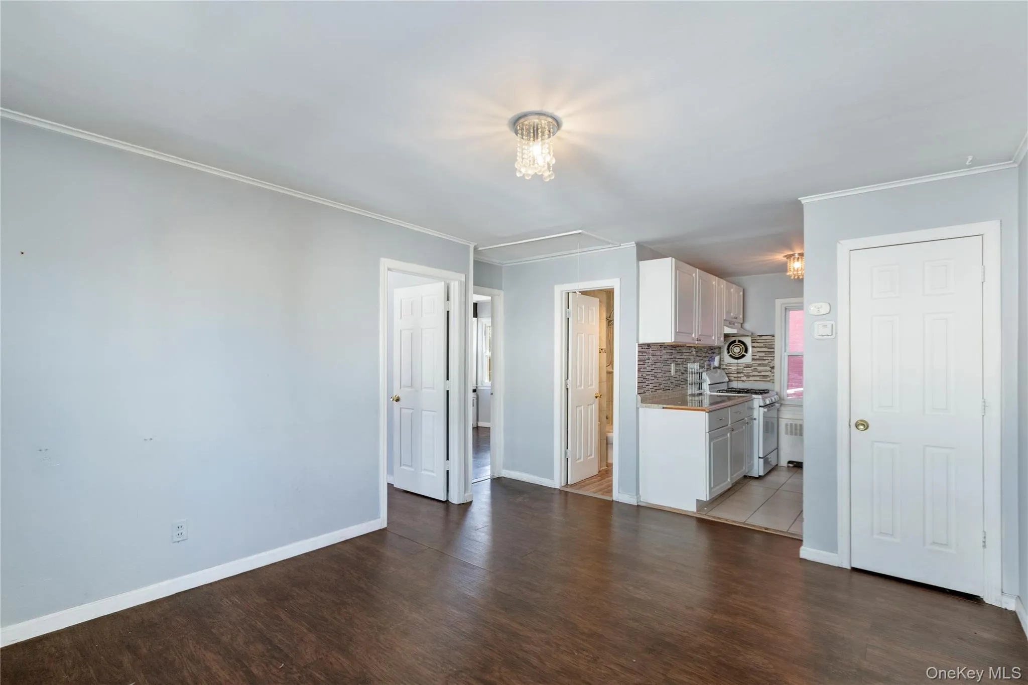 Unfurnished living room with dark wood-type flooring, ornamental molding, and attic access Unfurnished living room with dark wood-type flooring, ornamental molding, and attic access