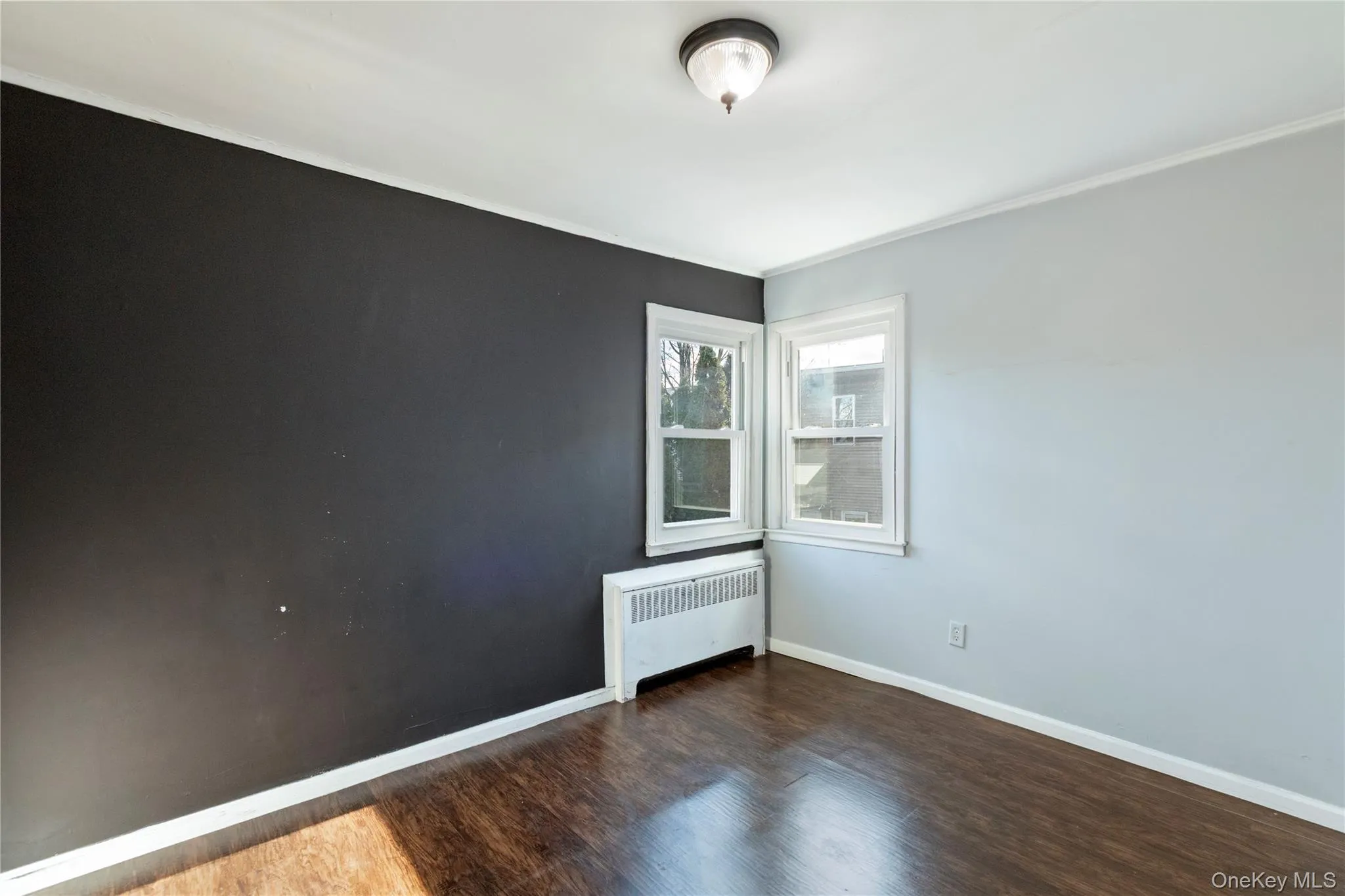Unfurnished room with radiator heating unit, dark wood finished floors, and crown molding Unfurnished room with radiator heating unit, dark wood finished floors, and crown molding