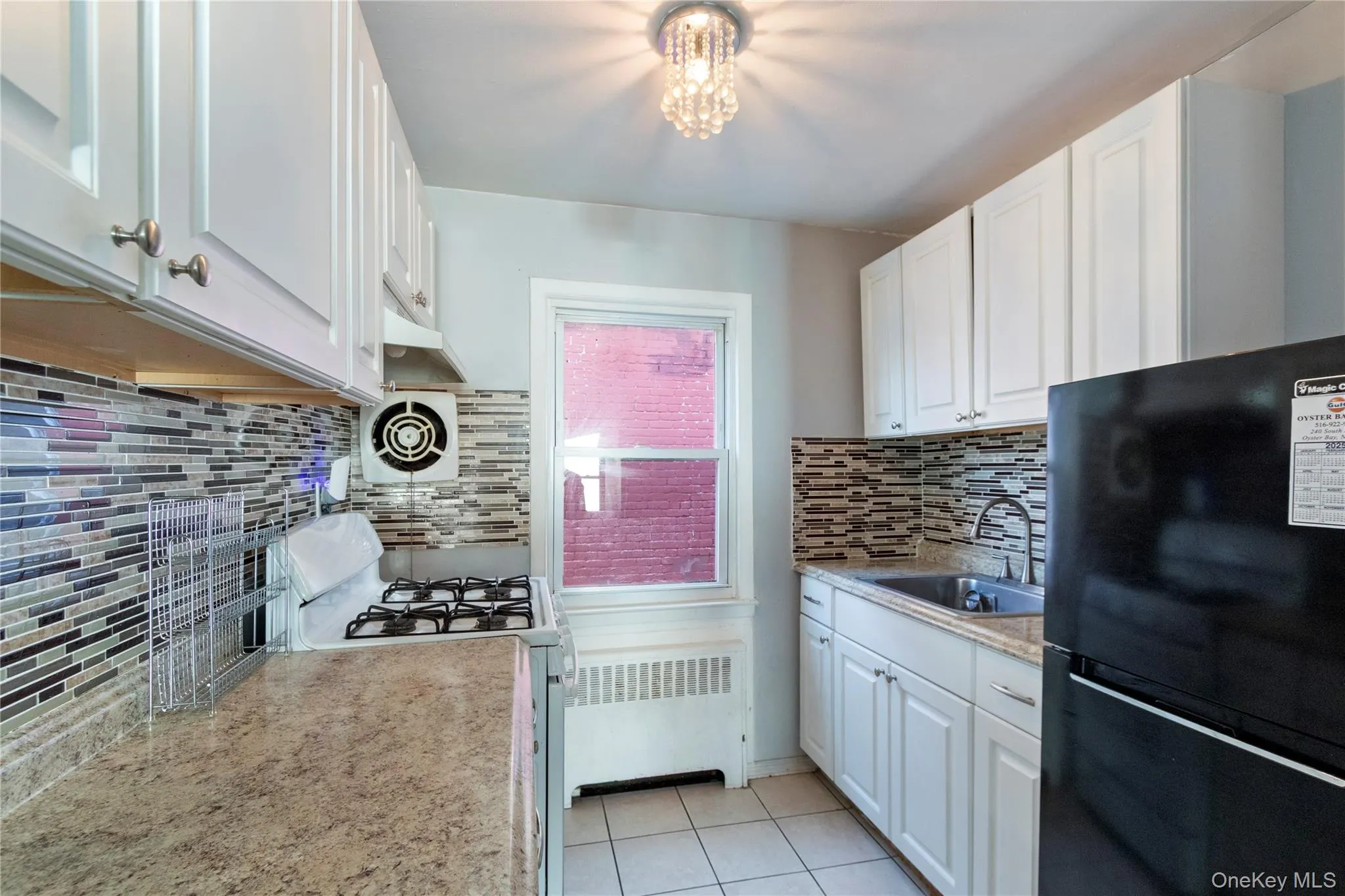 Kitchen featuring freestanding refrigerator, white gas range, white cabinets, radiator, and light tile patterned flooring Kitchen featuring freestanding refrigerator, white gas range, white cabinets, radiator, and light tile patterned flooring