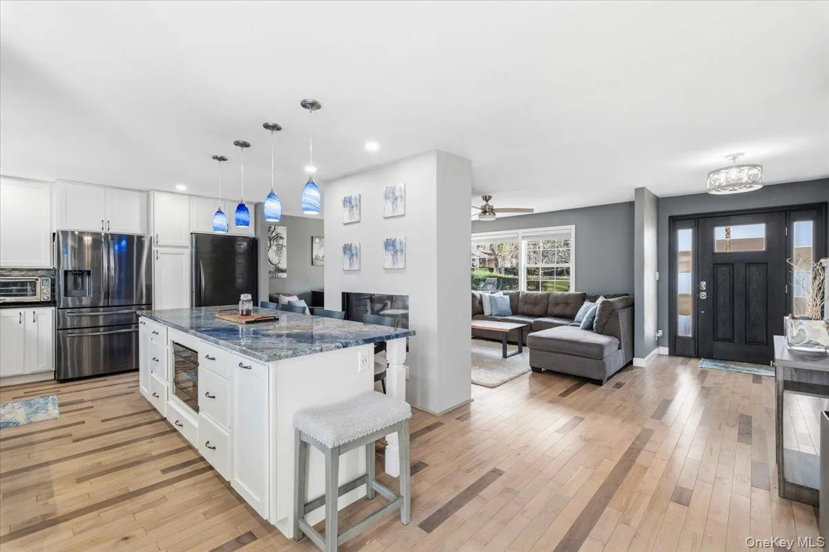 Kitchen featuring a kitchen bar, open floor plan, dark stone countertops, stainless steel fridge with ice dispenser, and white cabinetry Kitchen featuring a kitchen bar, open floor plan, dark stone countertops, stainless steel fridge with ice dispenser, and white cabinetry