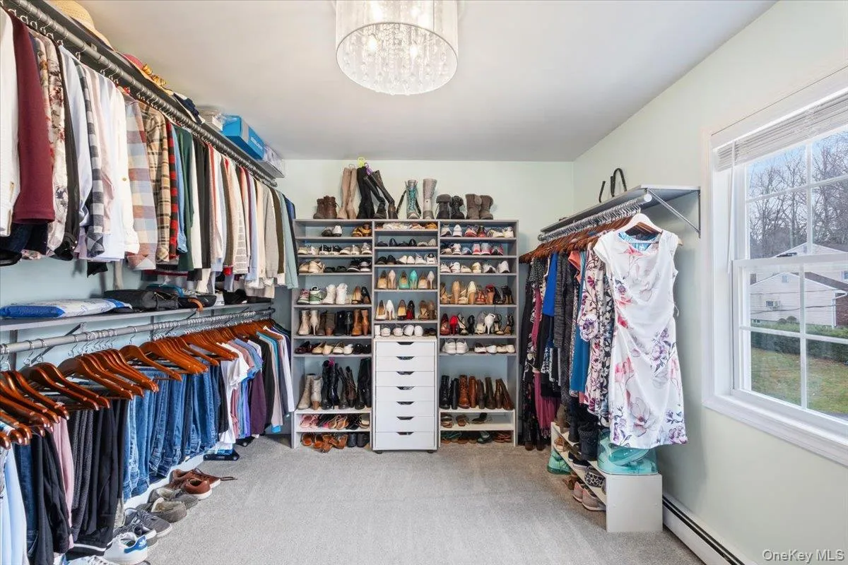 Walk in closet with a baseboard heating unit, light colored carpet, and a chandelier Walk in closet with a baseboard heating unit, light colored carpet, and a chandelier