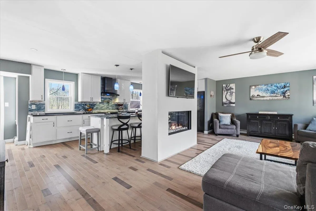 Living area featuring a glass covered fireplace, light wood finished floors, and ceiling fan Living area featuring a glass covered fireplace, light wood finished floors, and ceiling fan