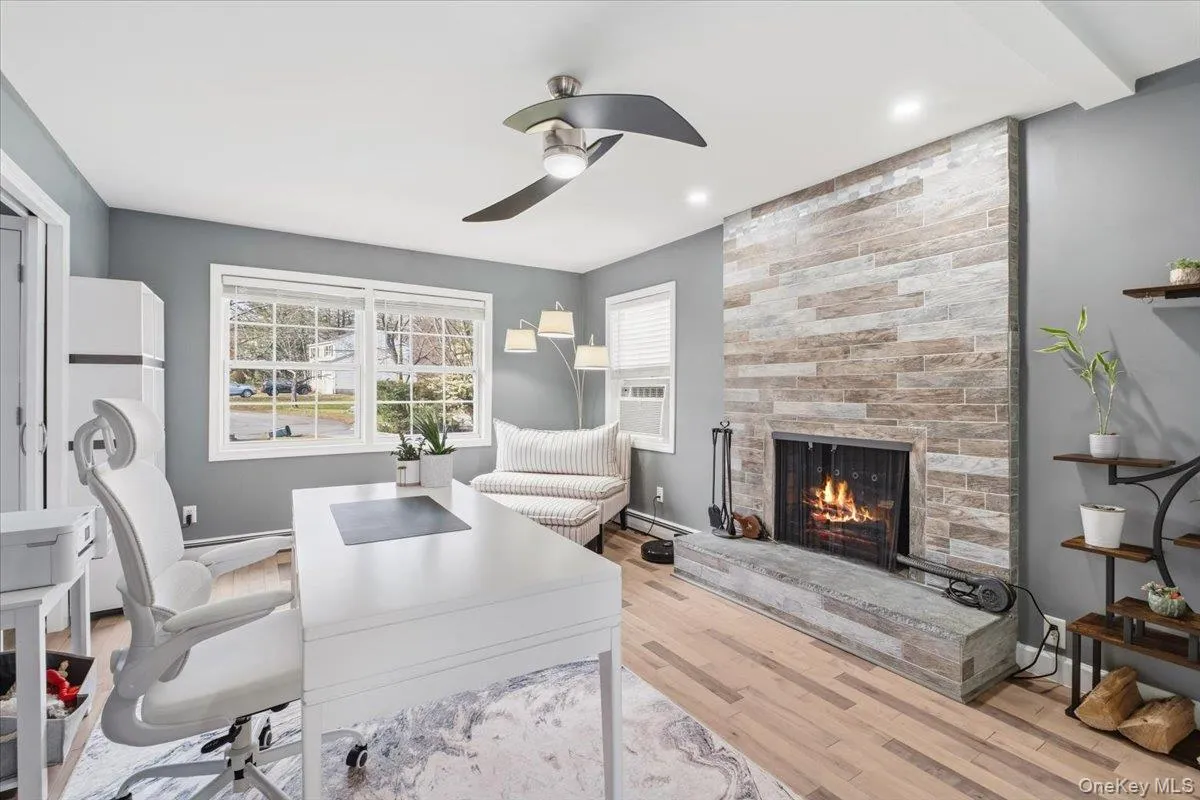 Office space featuring a fireplace, light wood-style flooring, a ceiling fan, a baseboard radiator, and cooling unit Office space featuring a fireplace, light wood-style flooring, a ceiling fan, a baseboard radiator, and cooling unit