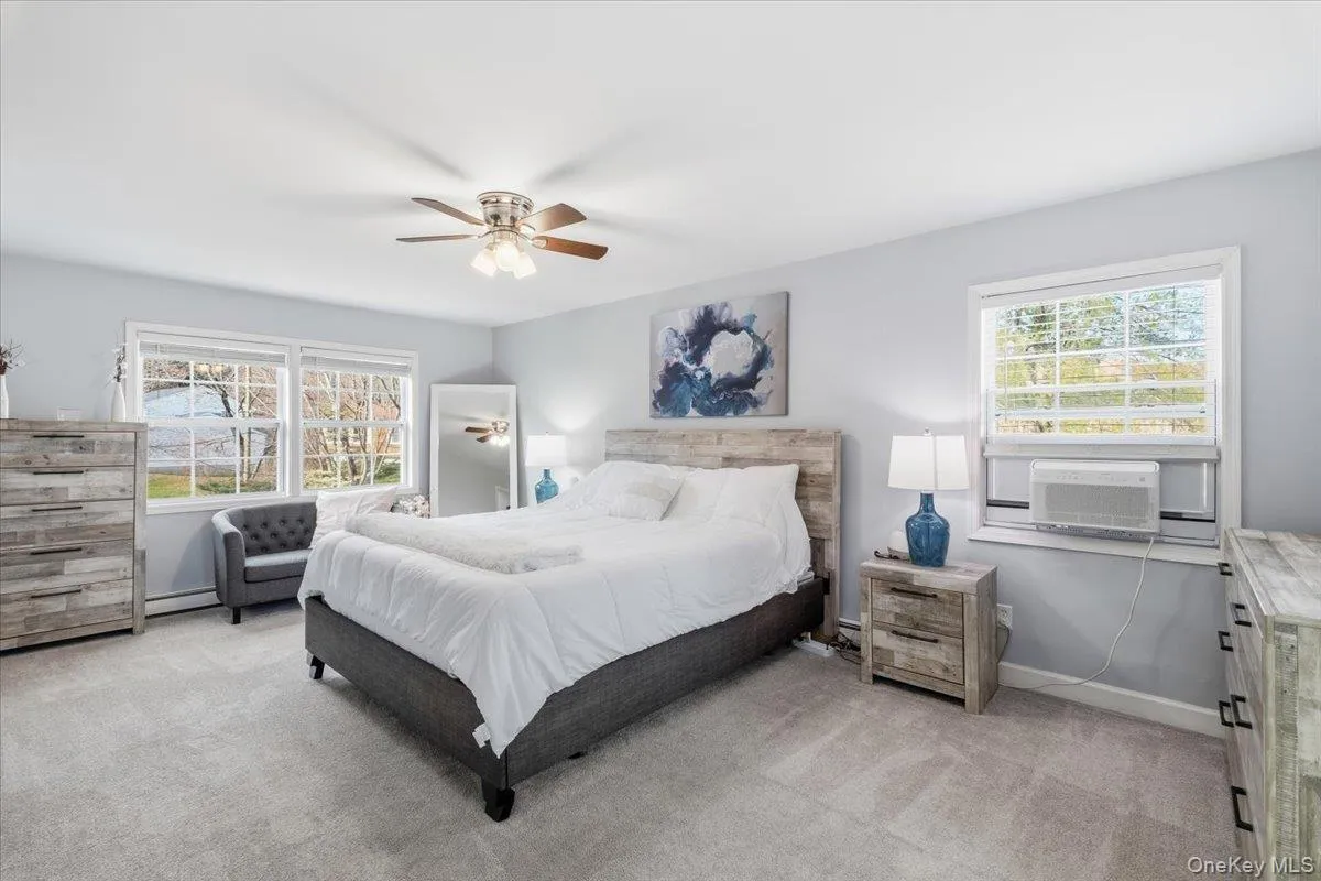 Bedroom featuring light colored carpet, a ceiling fan, multiple windows, and a baseboard radiator Bedroom featuring light colored carpet, a ceiling fan, multiple windows, and a baseboard radiator