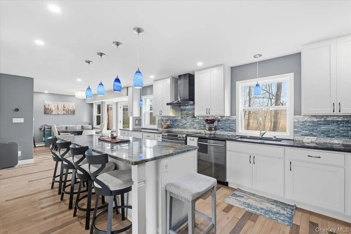 Kitchen with decorative light fixtures, white cabinetry, a kitchen bar, a spacious island, and dark stone counters Kitchen with decorative light fixtures, white cabinetry, a kitchen bar, a spacious island, and dark stone counters