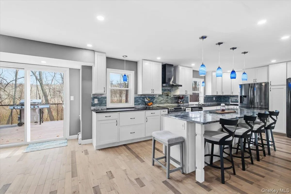 Kitchen with a breakfast bar, light wood-type flooring, hanging light fixtures, white cabinetry, and a center island Kitchen with a breakfast bar, light wood-type flooring, hanging light fixtures, white cabinetry, and a center island