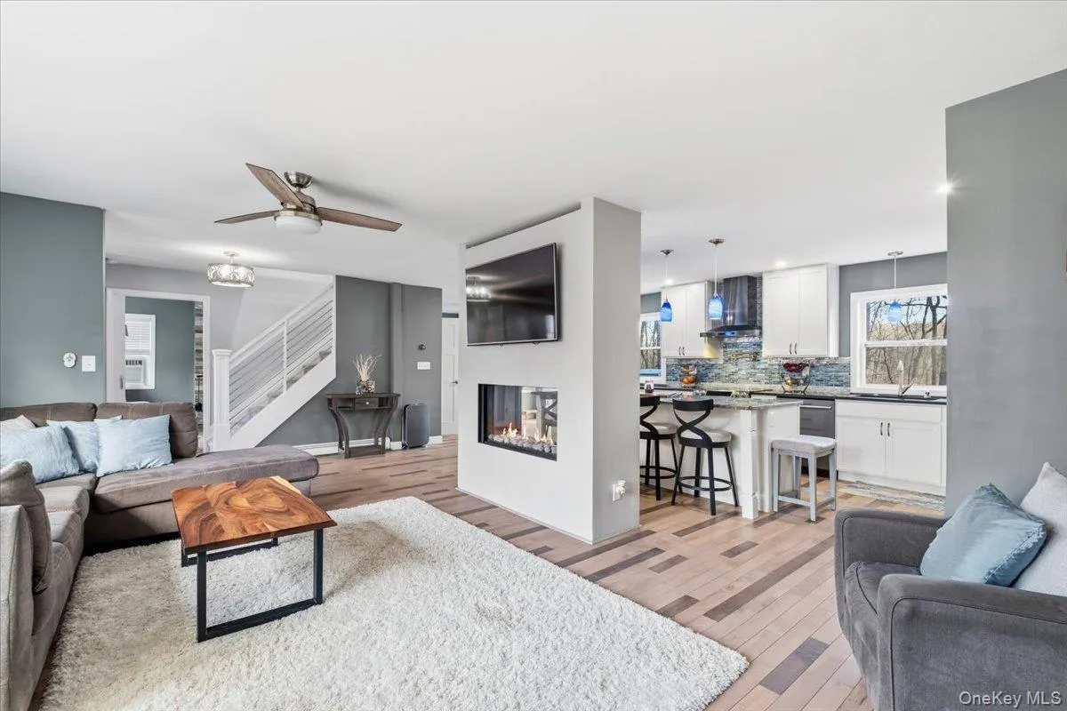 Living area featuring stairway, light wood finished floors, a glass covered fireplace, and a ceiling fan Living area featuring stairway, light wood finished floors, a glass covered fireplace, and a ceiling fan