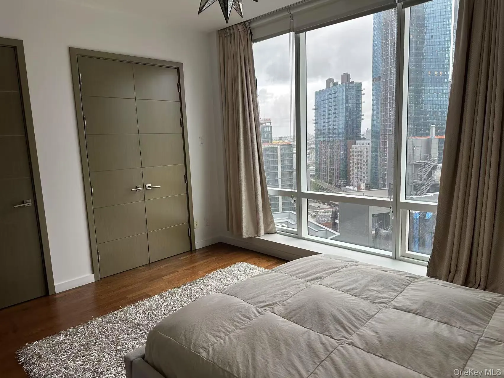 Bedroom featuring wood finished floors, two closets, a city view, and a wall of windows Bedroom featuring wood finished floors, two closets, a city view, and a wall of windows
