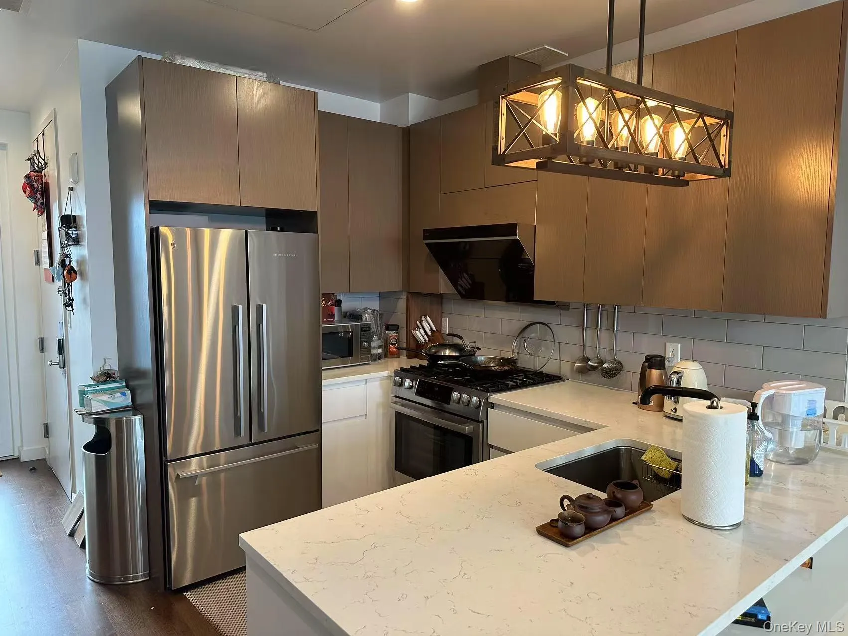 Kitchen with appliances with stainless steel finishes, light stone counters, decorative light fixtures, backsplash, and range hood Kitchen with appliances with stainless steel finishes, light stone counters, decorative light fixtures, backsplash, and range hood