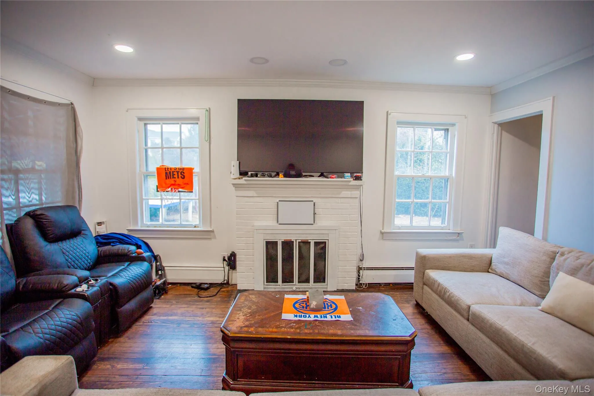 Living room with crown molding, wood-type flooring, plenty of natural light, a baseboard radiator, and a fireplace Living room with crown molding, wood-type flooring, plenty of natural light, a baseboard radiator, and a fireplace