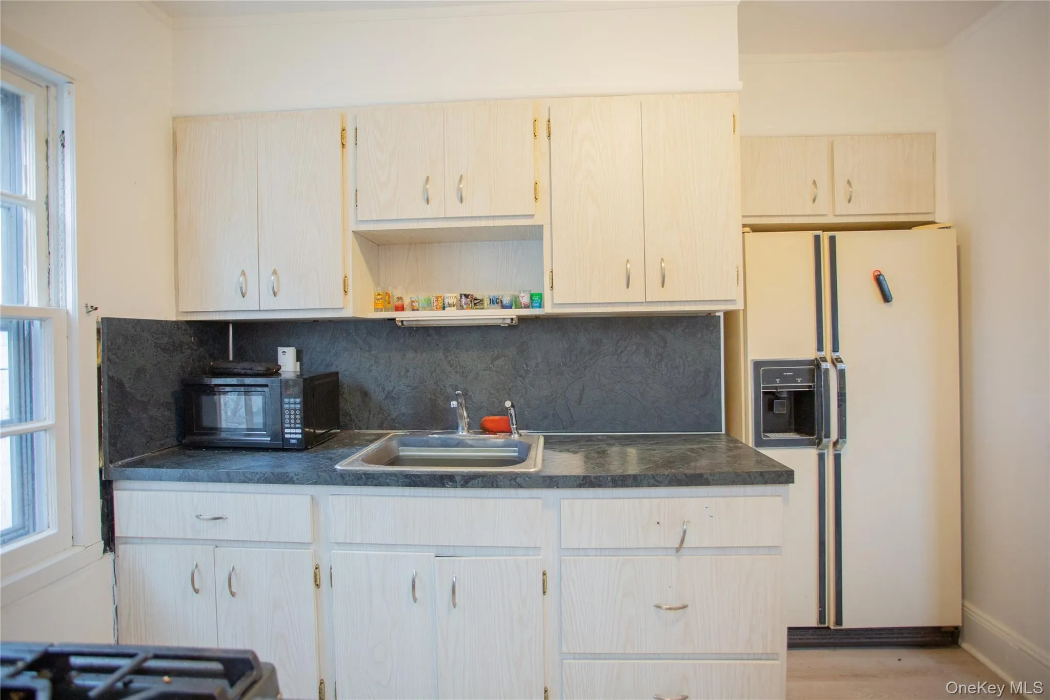 Kitchen with white fridge with ice dispenser, dark countertops, tasteful backsplash, open shelves, and plenty of natural light Kitchen with white fridge with ice dispenser, dark countertops, tasteful backsplash, open shelves, and plenty of natural light