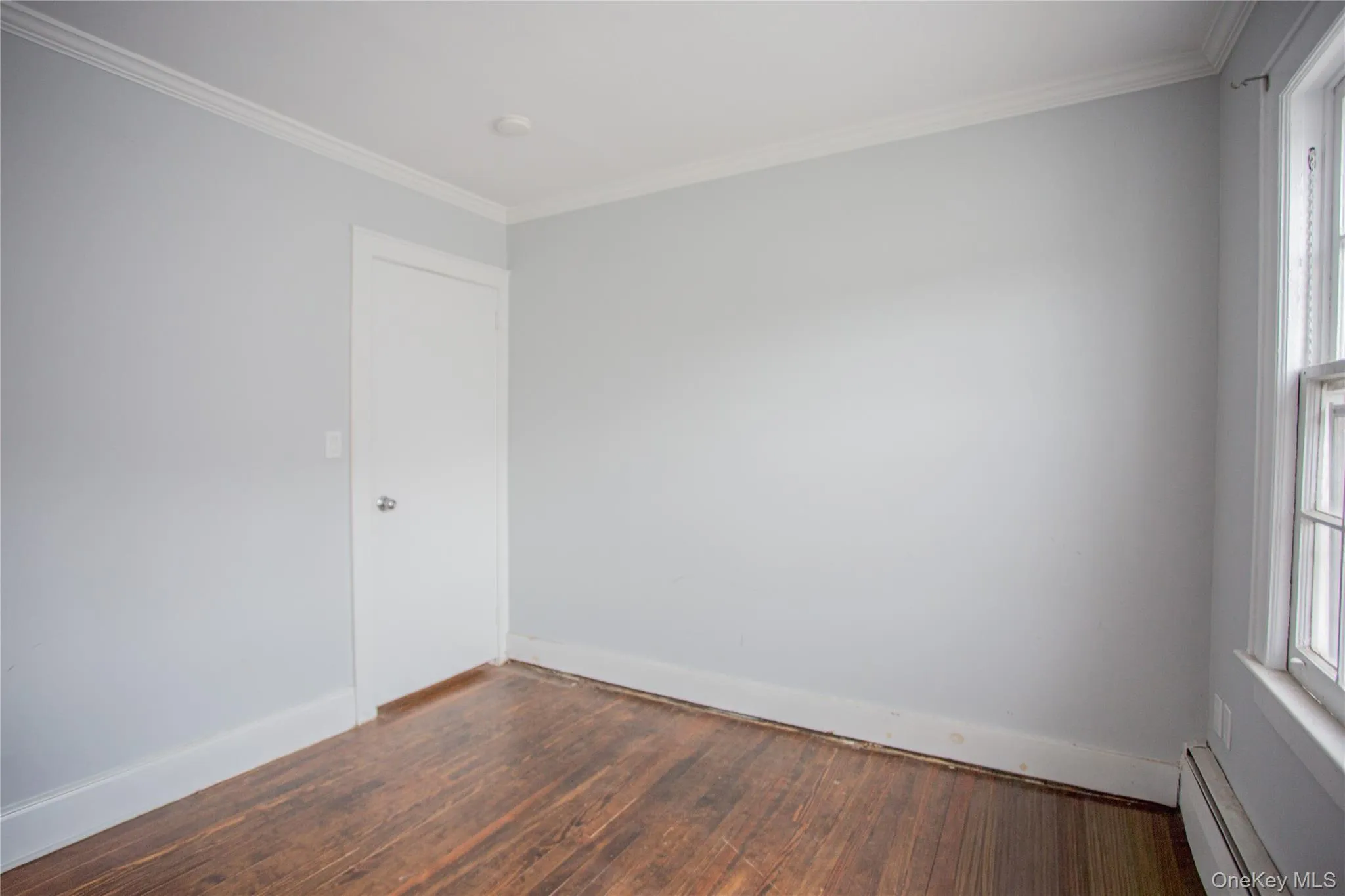 Unfurnished room featuring a baseboard heating unit, hardwood / wood-style floors, healthy amount of natural light, and ornamental molding Unfurnished room featuring a baseboard heating unit, hardwood / wood-style floors, healthy amount of natural light, and ornamental molding