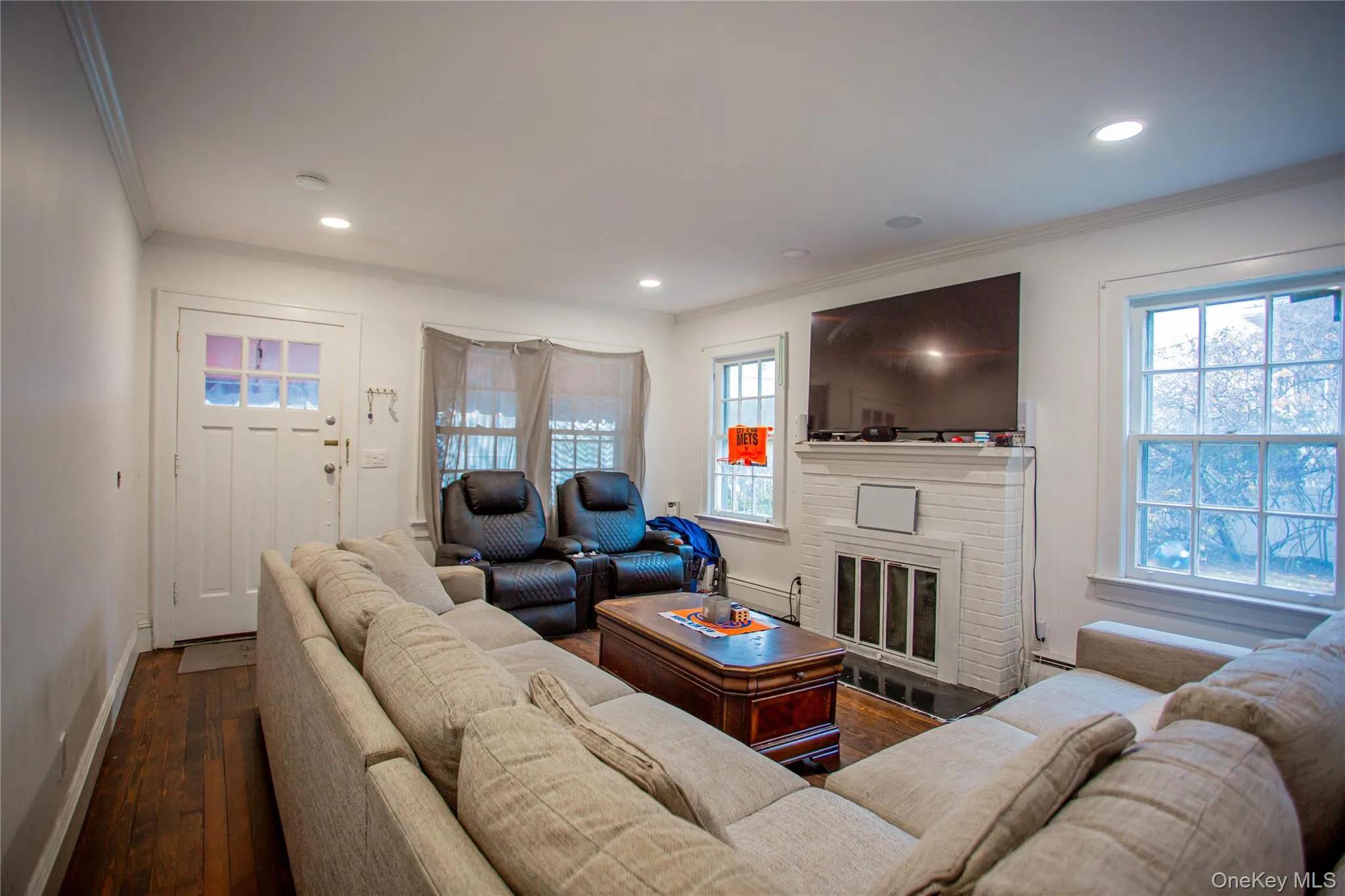 Living area with dark wood-style flooring, crown molding, a fireplace, recessed lighting, and a baseboard radiator Living area with dark wood-style flooring, crown molding, a fireplace, recessed lighting, and a baseboard radiator