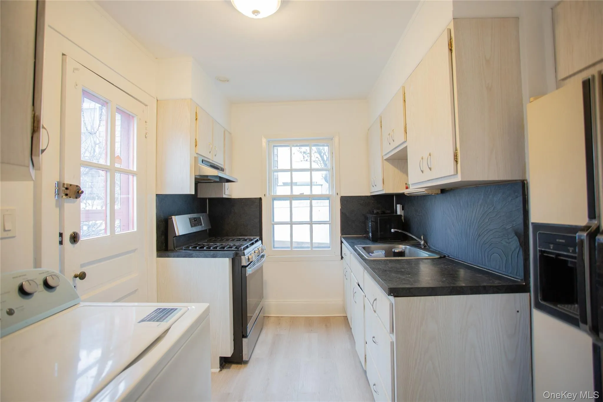 Kitchen with washer / dryer, stainless steel gas stove, white fridge with ice dispenser, light brown cabinetry, and tasteful backsplash Kitchen with washer / dryer, stainless steel gas stove, white fridge with ice dispenser, light brown cabinetry, and tasteful backsplash