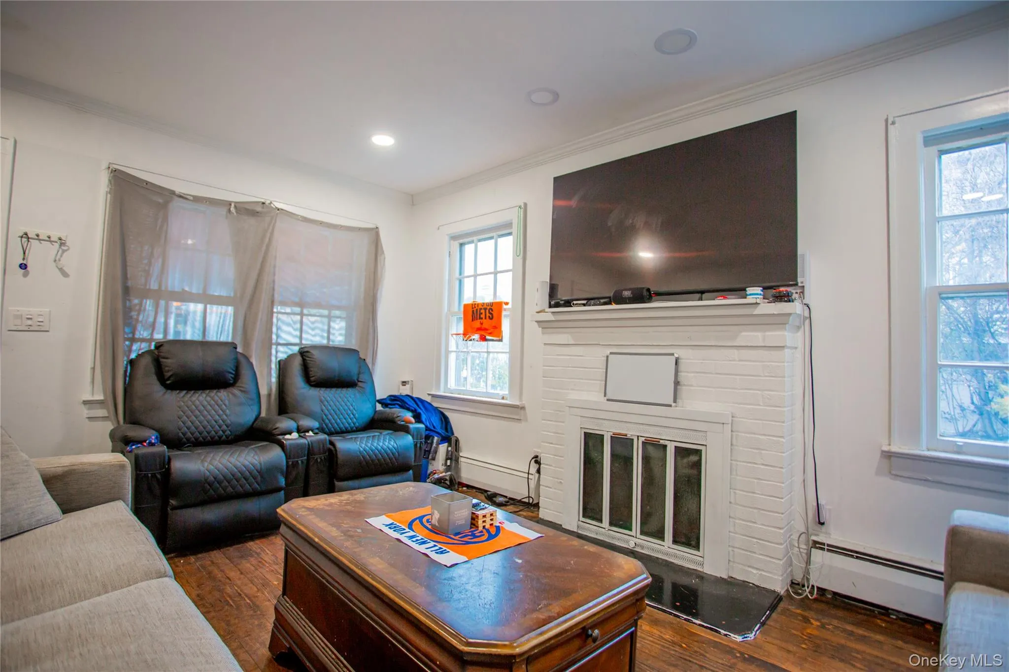 Living room with dark wood-style floors, baseboard heating, ornamental molding, a fireplace, and recessed lighting Living room with dark wood-style floors, baseboard heating, ornamental molding, a fireplace, and recessed lighting